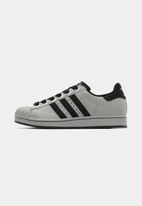 Gray leather sneakers with black suede accents, three black stripes, rubber toe cap, and round black laces. Low profile design.