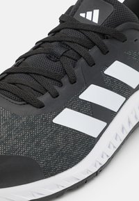 Black athletic shoe with textured fabric upper, white three-stripe logo, rubber sole, and round laces. Features reinforced toe cap.