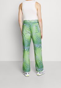 Zelené a modré kalhoty s širokými nohavicemi a vysokým pasem, s kapsami na zadní straně a hladkým povrchem. Nosené s šedými a žlutými teniskami.