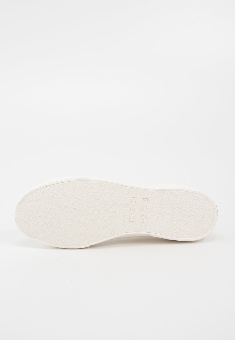 Suela de una zapatilla blanca con un fondo texturizado y una impresión rectangular del logo que dice "Tommy Jeans" centrada en la suela.