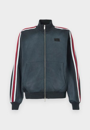 Navy zip-up jacket with high collar, featuring red and white striped accents on sleeves, two front pockets, and a small logo patch.