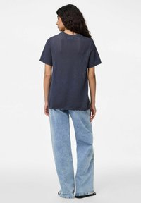 Námořnická modrá pletená blůza s krátkými rukávy, s texturovaným vzorem a zvlněným lemem, v kombinaci se světlými modrými širokými džíny.