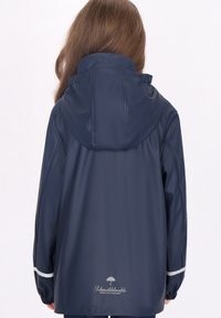 Jūros kariuomenės vandeniui atspari striukė su gobtuvu, elastingais rankogaliais ir atspindinčiais akcentais; glotni tekstūra; logotipas spausdintas apatėje nugaros dalyje.