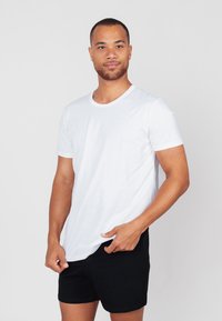 Weißes Baumwoll-T-Shirt mit Rundhalsausschnitt und kurzen Ärmeln; kombiniert mit schwarzen Shorts. Glatte Textur, lockere Passform, schlichtes Design.