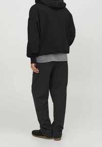 Felpa nera over-size con cappuccio regolabile, abbinata a una maglia grigia a strati e pantaloni neri larghi. Tessuto morbido, vestibilità comoda.