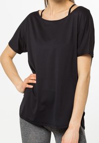 Camiseta deportiva negra de manga corta hecha de tela ligera y texturizada, con un escote amplio y detalles sutiles en las tiras de los hombros.