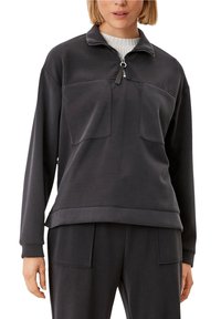 Pullover grigio scuro con collo a metà zip, due tasche frontali e una consistenza morbida. Presenta polsini e orlo a coste per una vestibilità rilassata.