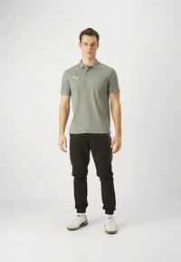 Pilkas polo marškinėlis su apykakle ir trumpomis rankovėmis, kuriame yra baltas logotipas. Derinamas su juodomis siaurėjančiomis kelnėmis ir baltais batais su rudu padu.