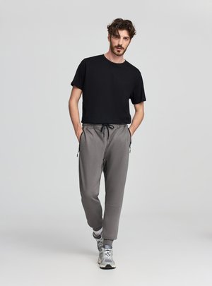T-shirt nera a maniche corte abbinata a pantaloni jogger grigi con tasche laterali e vita elastica. Modello con sneakers grigie.