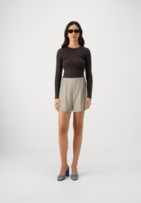 Black long-sleeve top paired with light-colored, striped shorts. Model wears dark sunglasses and blue heeled sandals.