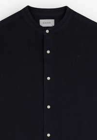 Camisa de lino azul marino con cuello de banda, que presenta una tapeta delantera con botones blancos y un sutil logo bordado en el pecho.