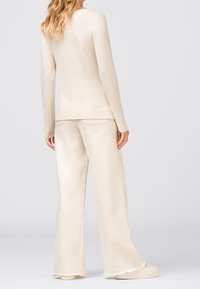 Beżowa bluzka z długim rękawem i pasujące szerokie spodnie z miękkiego materiału, o luźnym kroju i postrzępionych brzegach spodni.