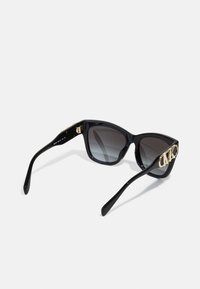 Ochelari de soare negri cu formă de ochi de pisică și lentile degradate. Au un accent cu logo auriu pe lateral și un cadru din plastic lucios, elegant.