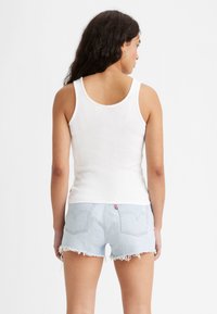 Hvid ribbet tanktop iført med lyseblå denimshorts med slidser og baglommer. Shortsene har et rødt logoetikette.