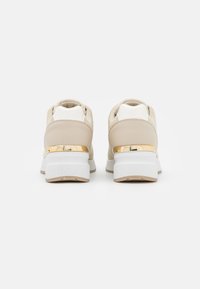 Béžové tenisky s texturovaným svrškem, bílou podešví a zlatým akcentem na patě. Zaoblený design s polstrovaným interiérem pro pohodlí.