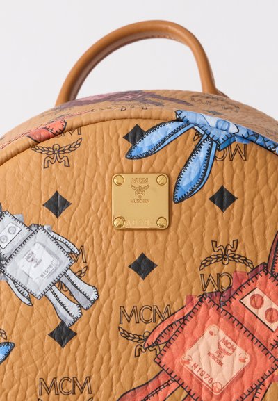 Τσάντα πλάτης από ταμπά δέρμα με πολύχρωμες τυπωμένες καρικατούρες, χρυσή πλακέτα με λογότυπο και αντίθετες ραφές. Στρογγυλό σχήμα με χειρολαβή στην κορυφή.