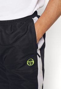 Svarta sportshorts med vita sidestreck, tillverkade av andningsbart material. Har en liten grön logotyp på vänster ben och sidoficka.