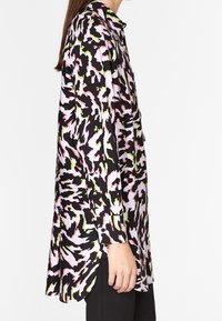 Pitkähihaisen paidan musta, vaaleanpunainen ja limenvihreä abstrakti kuvio; sileä kangas; kaareva helma; yksi nappi hihassa; löysä malli.