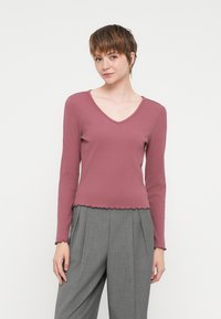 Ριγέ μακρυμάνικο τοπ σε ήπιο ροζ, με V-λαιμόκοψη και κομψό τελείωμα. Συνδυάζεται με γκρι παντελόνι με ψηλή μέση και πτυχώσεις.