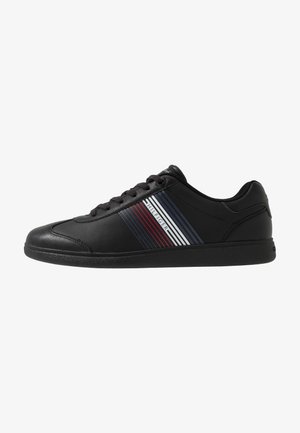 Sneaker nera con tomaia in pelle liscia, caratterizzata da strisce orizzontali in rosso, bianco e blu. Punta rotonda e design con lacci. Suola in gomma.