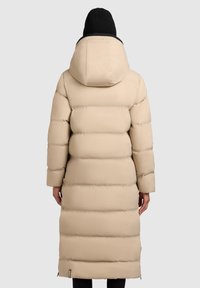 Smėlio spalvos, ilga pūkinė striukė su gaubtu, horizontaliomis siūtomis juostomis, lygiu paviršiumi ir logotipo detale apačioje.