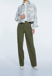 Veste à carreaux grise et blanche taillée avec fermeture à boutons, associée à un pantalon taille haute en olive avec plis avant et détail de bouton.