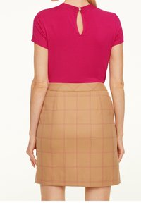 Dopasowany różowy top z wycięciem z tyłu, w połączeniu z mini spódnicą w brązową kratę, z różowymi przeszyciami i wysokim stanem.