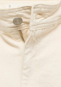 Jean en denim beige avec une fermeture à bouton métallique, une fermeture éclair visible et des détails de couture. Le tissu présente une apparence lisse et texturée.