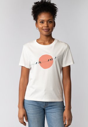 T-shirt en coton blanc avec un motif central représentant un cercle pêche avec des oiseaux perchés sur une ligne fine, col rond et manches courtes.