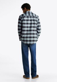 Camisa de franela de cuadros en azul, negro y blanco. Mangas largas, cuello estándar y dobladillo curvado. Combinada con jeans de mezclilla oscuros y zapatos.