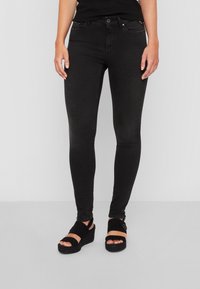 Jeans ajustados negros fabricados en denim con una textura suave, con un diseño clásico de cinco bolsillos y herrajes de metal en la parte frontal.