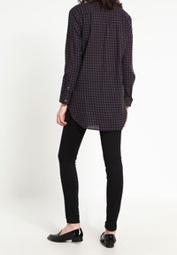 Camicia a maniche lunghe a quadri in toni scuri, con orlo curvo e polsini abbottonati, abbinata a pantaloni skinny neri e scarpe flat.