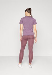 T-shirt de sport violet à texture et leggings assortis ; design ajusté, tissu lisse, longueur genou avec un éclat subtil. Des baskets blanches complètent le look.