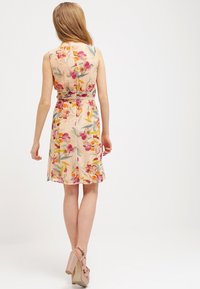Robe florale avec un fond pêche clair, présentant une taille cintrée, un design sans manches et des motifs de fleurs multicolores.