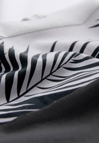 Černobílá tkanina s listovým vzorem, hladkým povrchem a kontrastním tmavým podkladem. Design obsahuje realistické palmové listy.