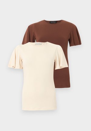 Deux hauts à manches courtes avec manches bouffantes, l'un crème et l'autre brun, présentés sur un fond clair uni.