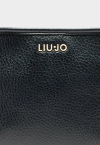 Must mustritud must nahast käekott sileda viimistlusega, millel on ees kõrgemal kohal kuldne "LIU.JO" logo.