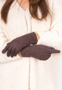 Braune Wildlederhandschuhe mit fünf Fingern, glatter Textur und enganliegendem Sitz, getragen von einer Person mit einer cremefarbenen, flauschigen Strickjacke.