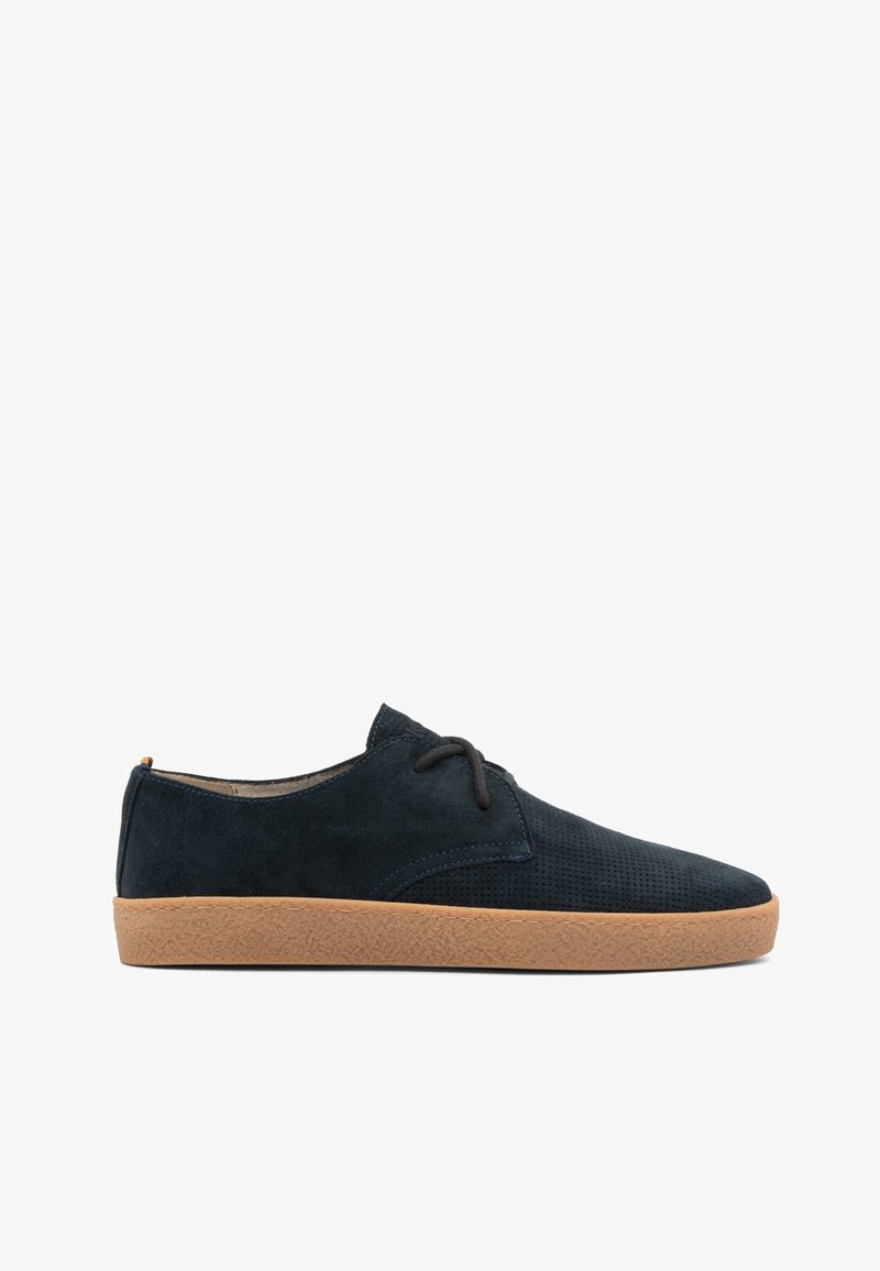 Chaussure à lacets en daim noir avec une texture perforée et une semelle en caoutchouc marron, vue de profil sur fond blanc.