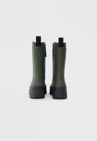 Bottes en caoutchouc vertes avec une finition texturée, dotées d'une semelle noire, de zips latéraux et de languettes à l'arrière pour un enfilage facile.