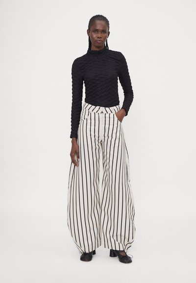 Black textured long-sleeve top with a fitted silhouette paired with high-waisted, wide-leg white pants featuring vertical black stripes.