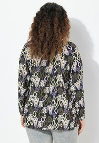 Camicia a maniche lunghe caratterizzata da un tessuto nero con motivi geometrici e floreali in verde, viola e bianco; texture morbida, vestibilità rilassata.