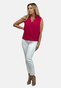 Fuksjowa bezrękawnikowa bluzka z kołnierzykiem, z zapinanym krojem i guzikami, połączona z białymi dopasowanymi spodniami i butami na obcasie w wężowy wzór.