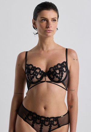 Ensemble de lingerie noire composé d'un tissu en maille transparente, de détails en dentelle florale complexe, de bonnets avec armatures et de sangles décoratives. Comprend des accents en métal doré.