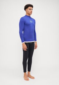Langt ermet blå rash guard med en tettsittende design og hvit aksent ved kanten, sammen med svarte tettsittende svømmeleggings.