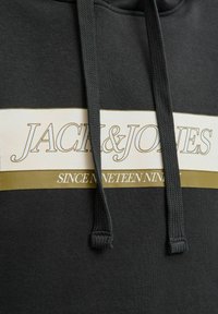 Sort hættebluse lavet af blødt stof, med en hvid og olivengrøn vandret stribe, der har teksten "JACK & JONES" og "SINCE NINETEEN NINETY."