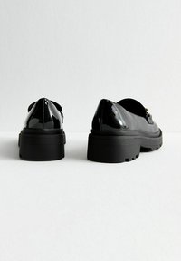 Scarpe in pelle verniciata nera con una suola nera spessa, dotate di punta arrotondata e una finitura liscia e lucida.