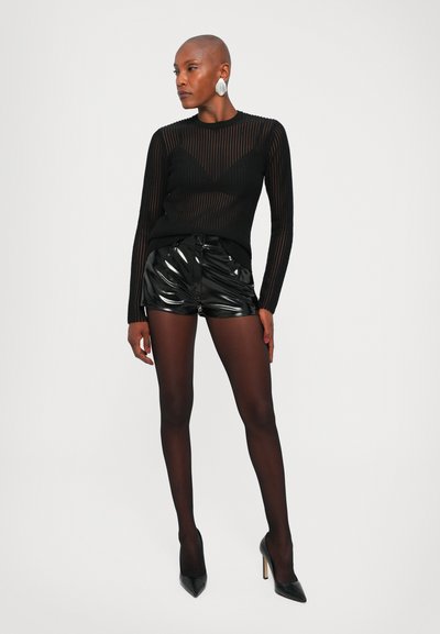 Black ribbed long-sleeve top, sheer design; shiny black vinyl shorts with front buttons; sheer black tights; black pointed heels; silver earring.