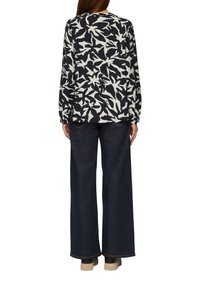 Langärmliges Top mit einem schwarz-weißen abstrakten Blumenmuster, kombiniert mit lässigen, weiten dunkelblauen Jeans und hellen Plateauschuhen.