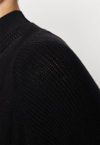 Maglione nero lavorato a maglia con collo a coste, motivo testurizzato e design aderente sulle spalle, con sezioni sottili a maglia aperta.